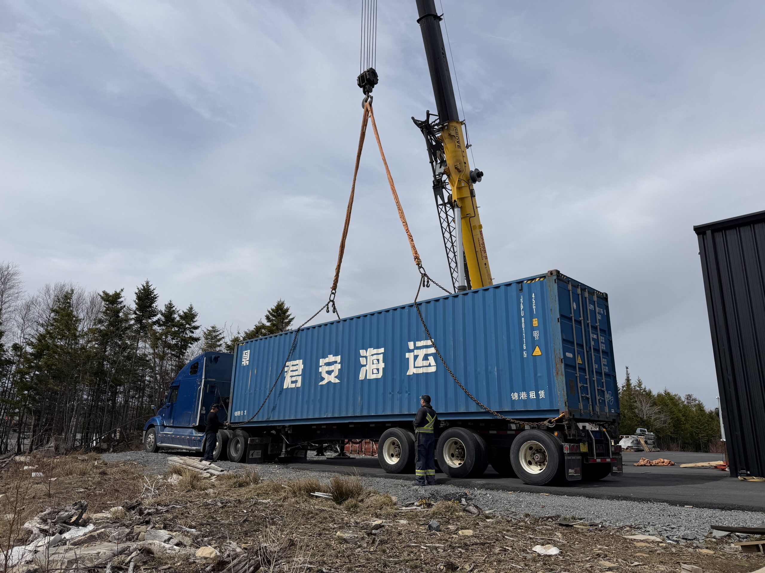 Crane lifting a shipping container from a Masic Transport truck at a customer site
